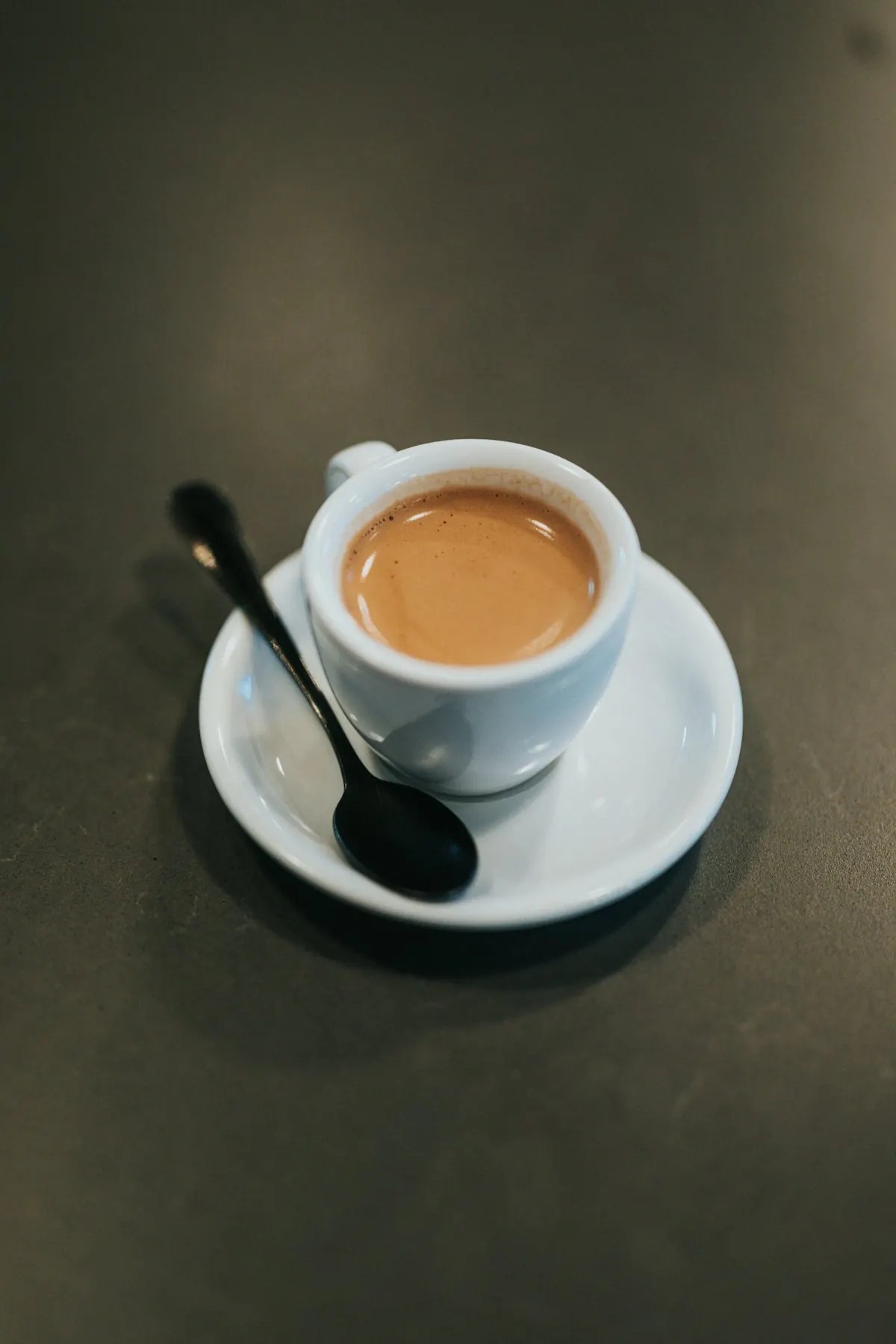 Espresso v beli skodelici s krožničkom na temni mizi